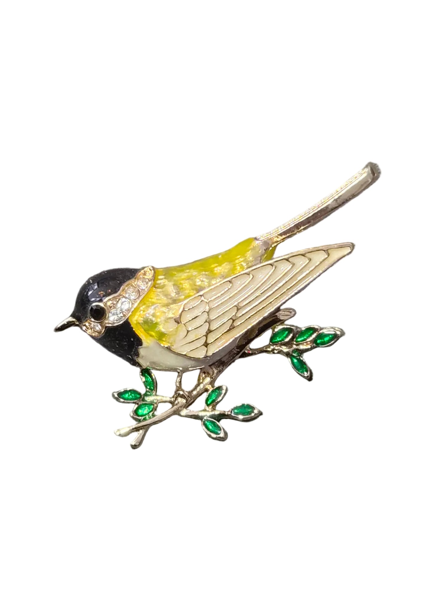 A bird-shaped enamel brooch perched on a small branch with green leaves.