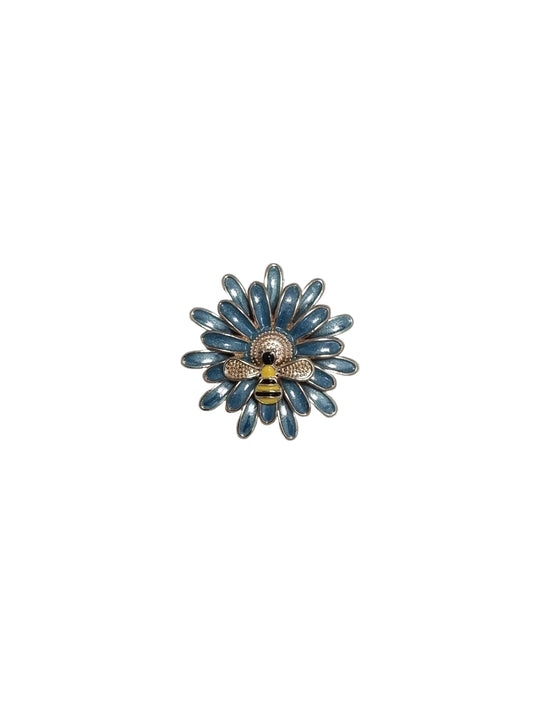 Decorative brooch with blue floral design and bee on a textured gray background