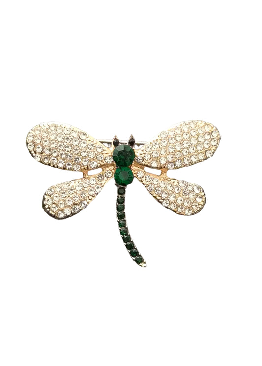 A dragonfly-shaped brooch with pavé-set clear stones on its wings and a green emerald-cut body and segmented green tail.