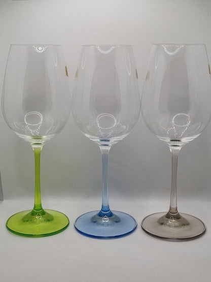 Set of three white wine glasses with blue, green and grey stems on a light grey background