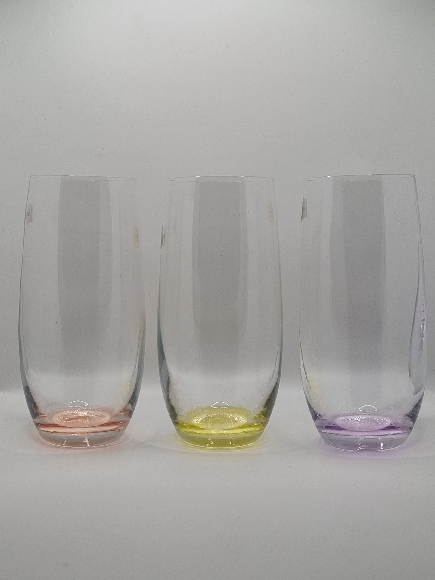 Set of three clear glass tumblers with red, yellow and purple base on a white background
