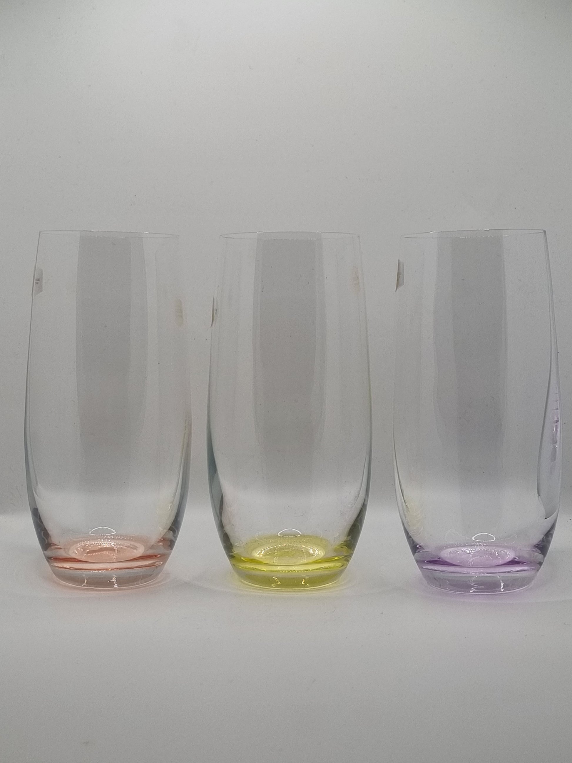 Set of three clear glass tumblers with red, yellow and purple base on a white background