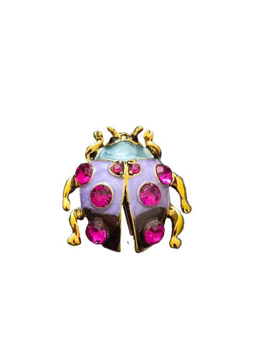 A ladybug-shaped brooch with gold-tone metal, a pale lavender body, and bright pink rhinestones.