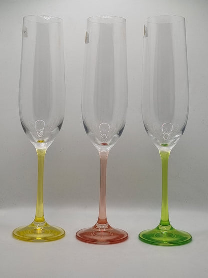 Set of three champagne flutes with yellow, red and green stems on a light gray background