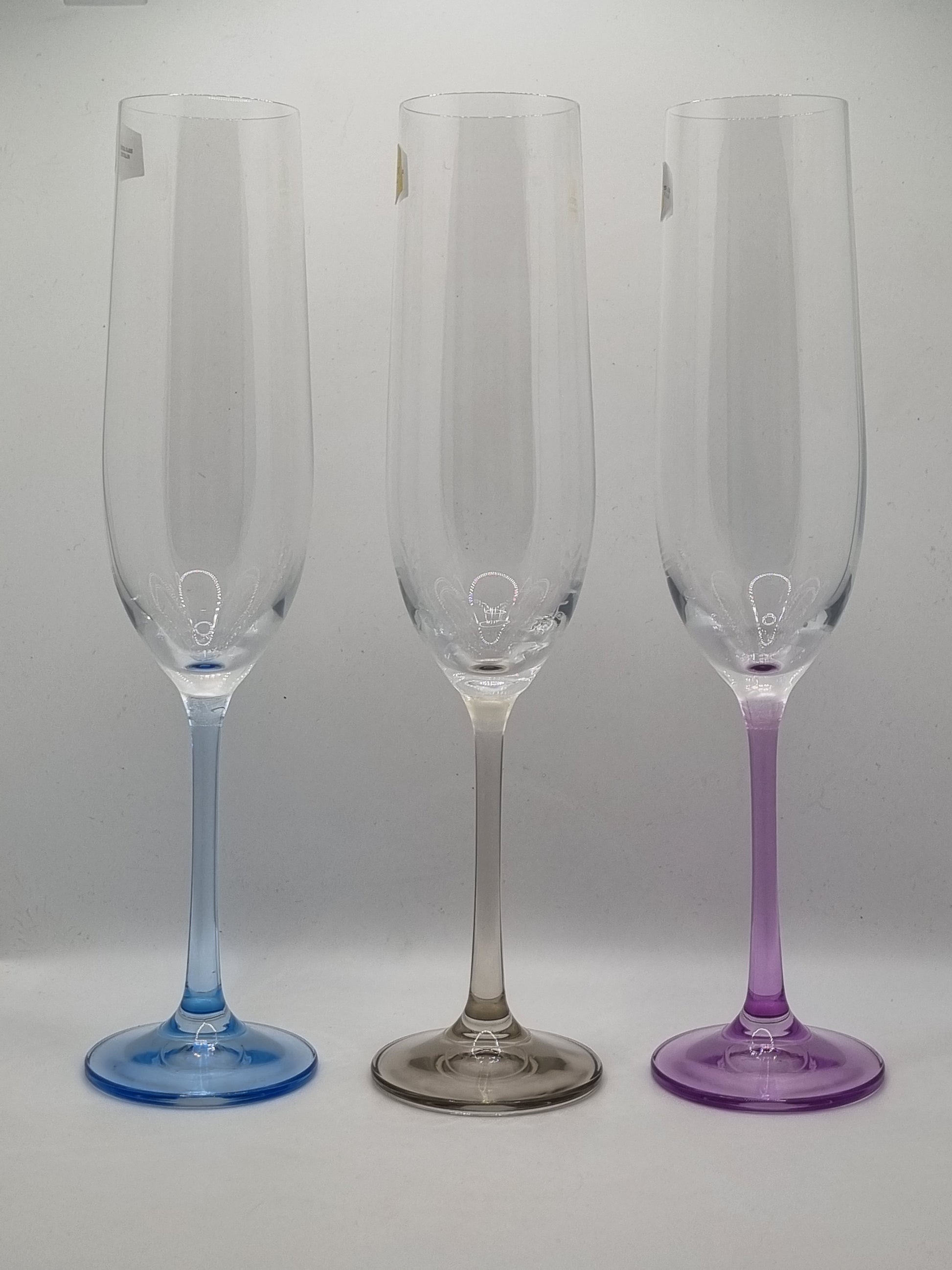 Set of three champagne flutes with blue, purple and grey stems on a light gray background