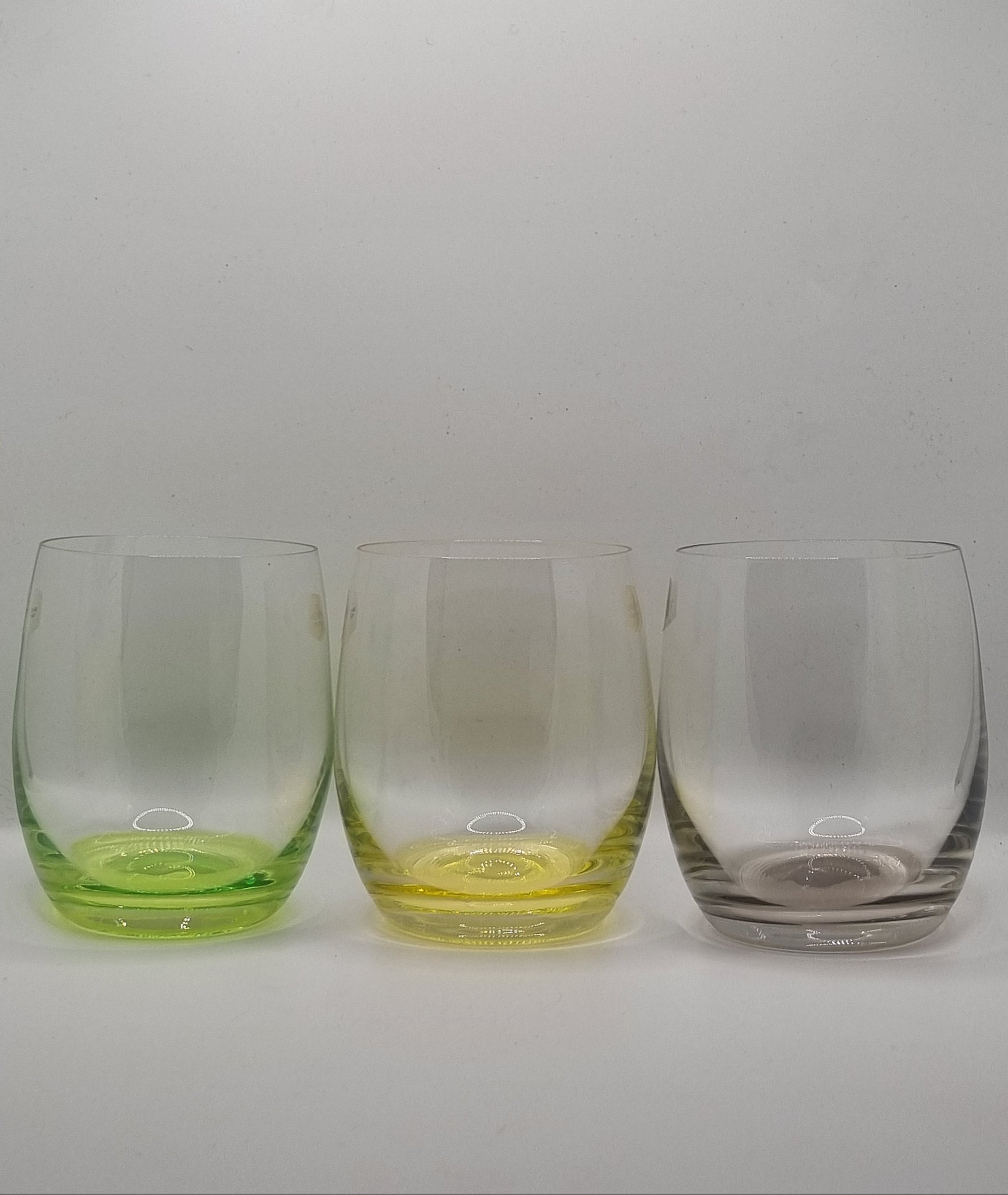 Set of three whiskey tumblers with green, yellow and grey bases on a light grey background