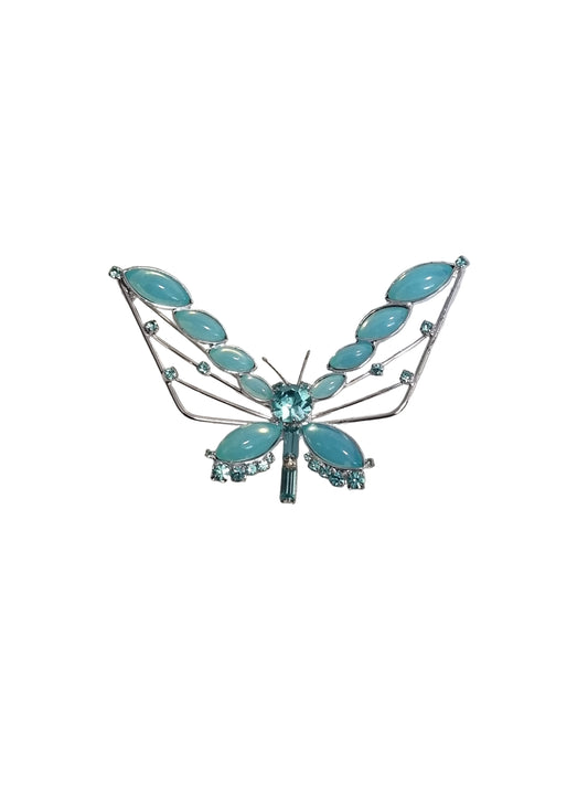 Dragonfly-shaped brooch with turquoise stones on a textured gray background