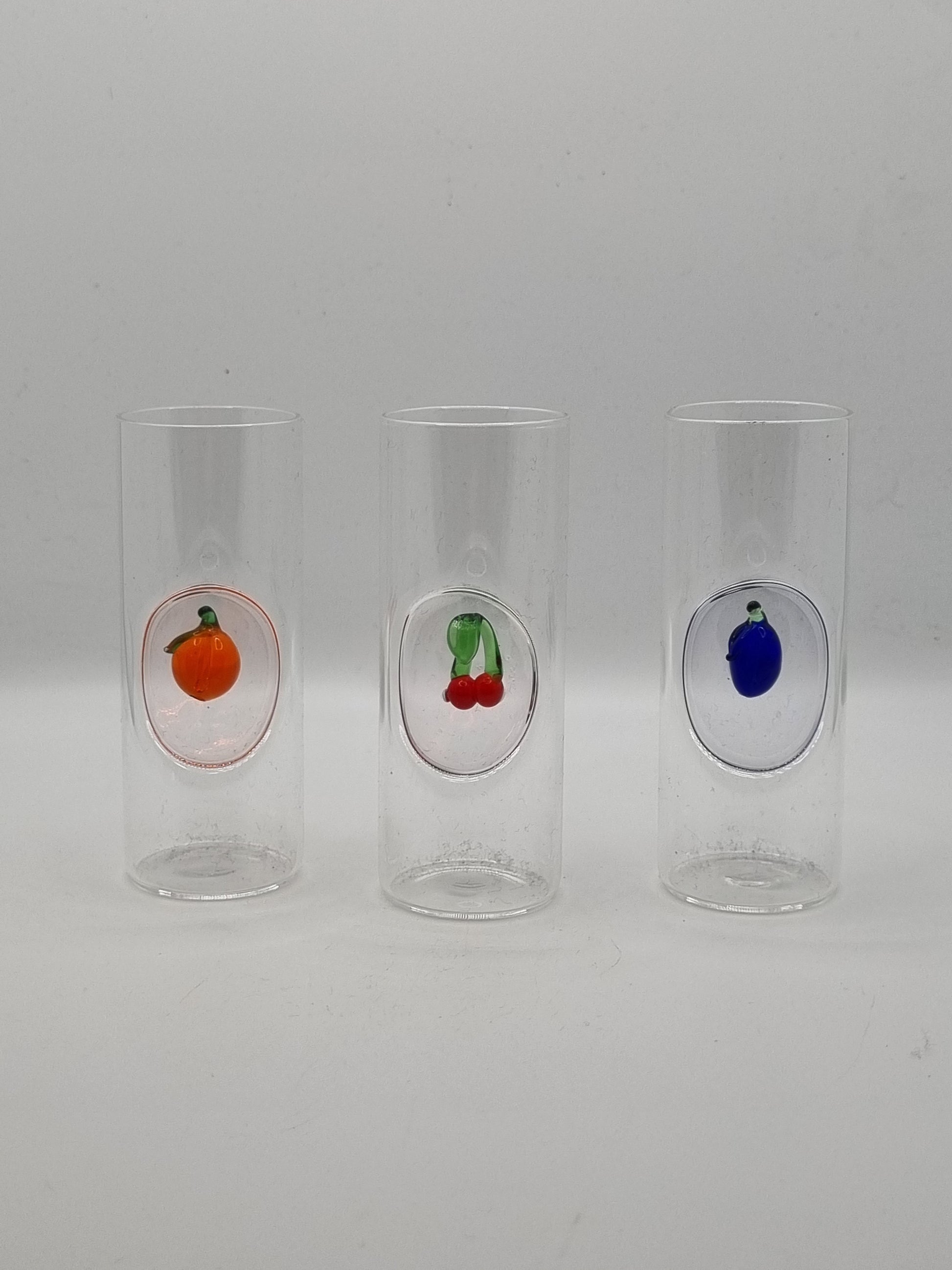 Three small round shot glass with colourful fruit insets - blue plum, red cherries and an orange