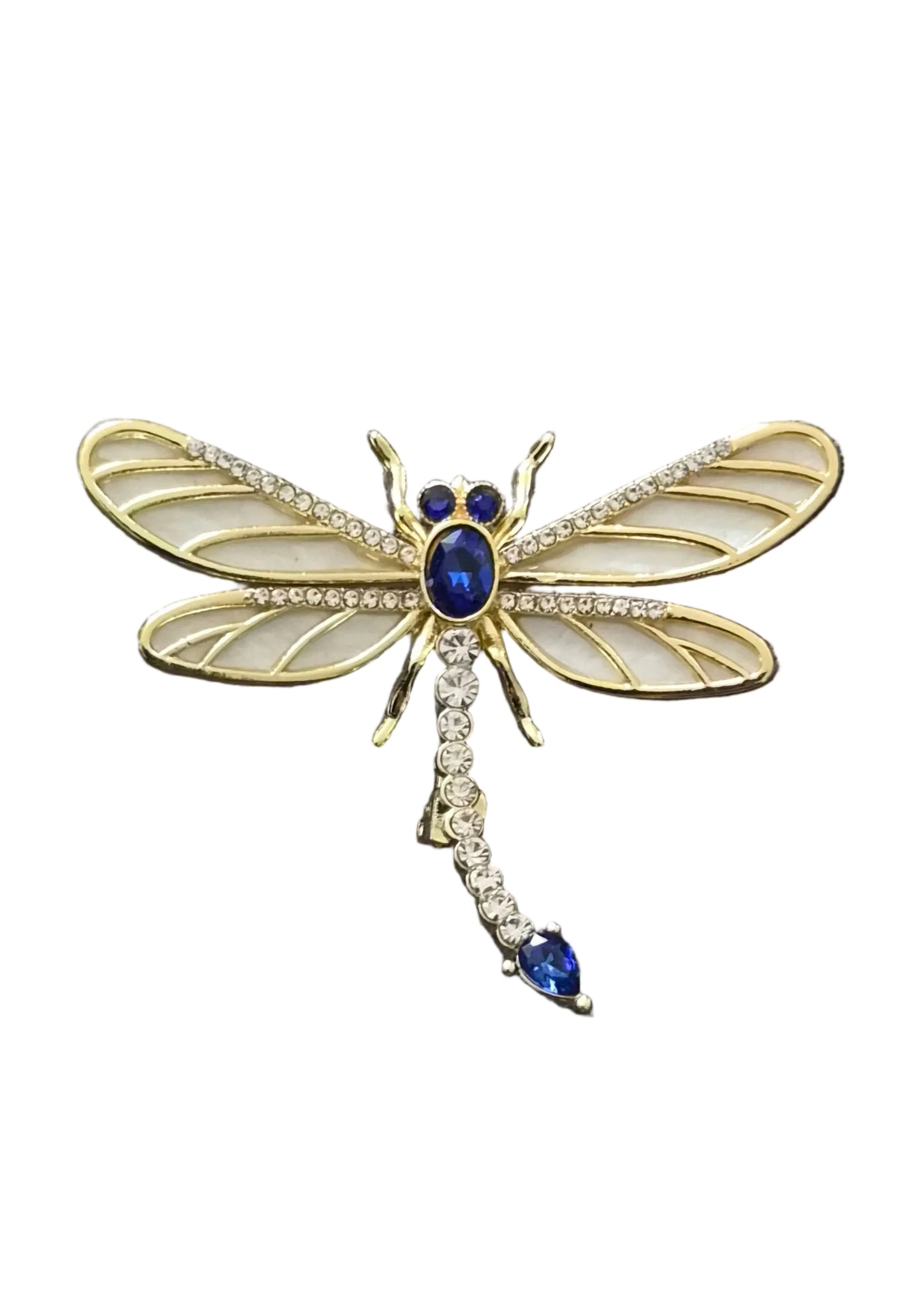 A gold dragonfly brooch with cream-colored wings, a blue gemstone body, and a tail adorned with clear crystals and a blue stone.
